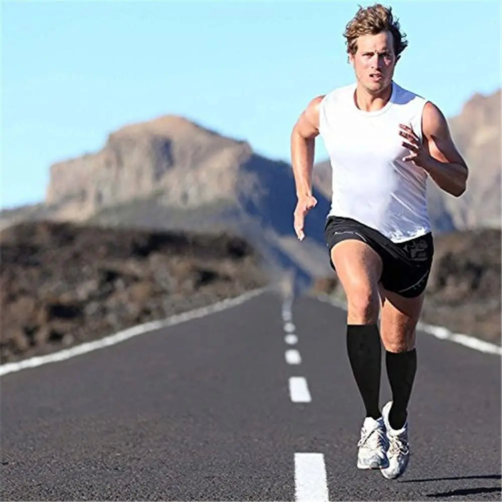 A male runner in a white tank top and black shorts is jogging down an asphalt road with mountains in the background.
