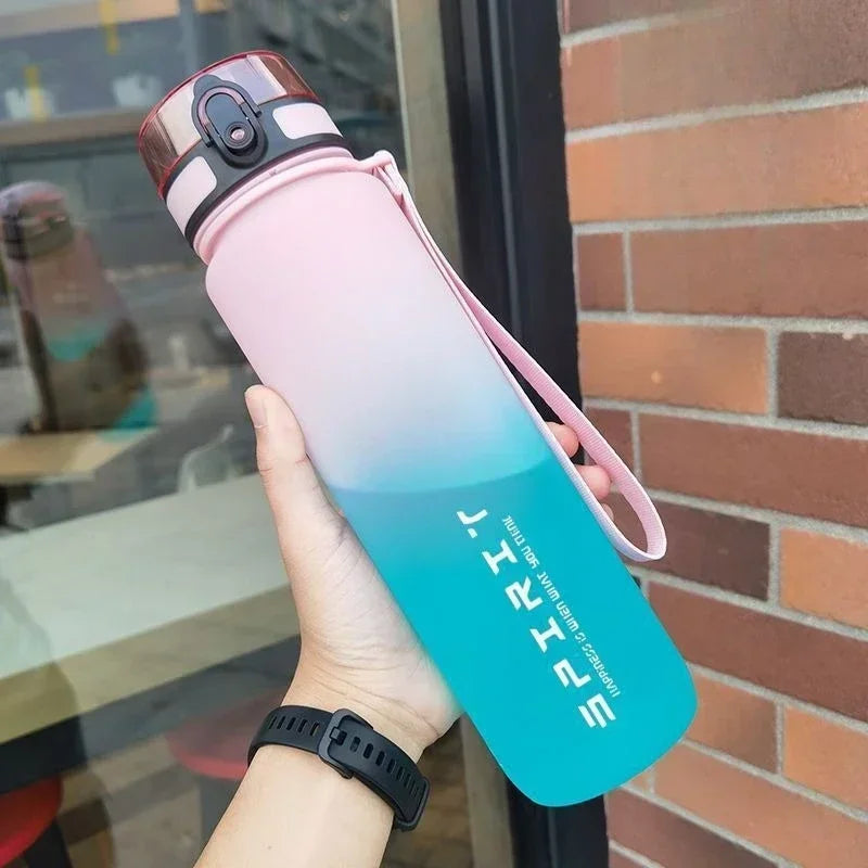 A hand holds a gradient insulated sports water bottle with pink and blue accents against a brick background.