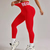 Eine Frau in roten, hoch taillierten, nahtlosen Yoga-Leggings und einem weißen Crop-Top steht auf einem hellgrauen Boden.