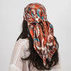 A woman wearing an orange and blue paisley silk shawl scarf tied around her neck, with long dark hair.