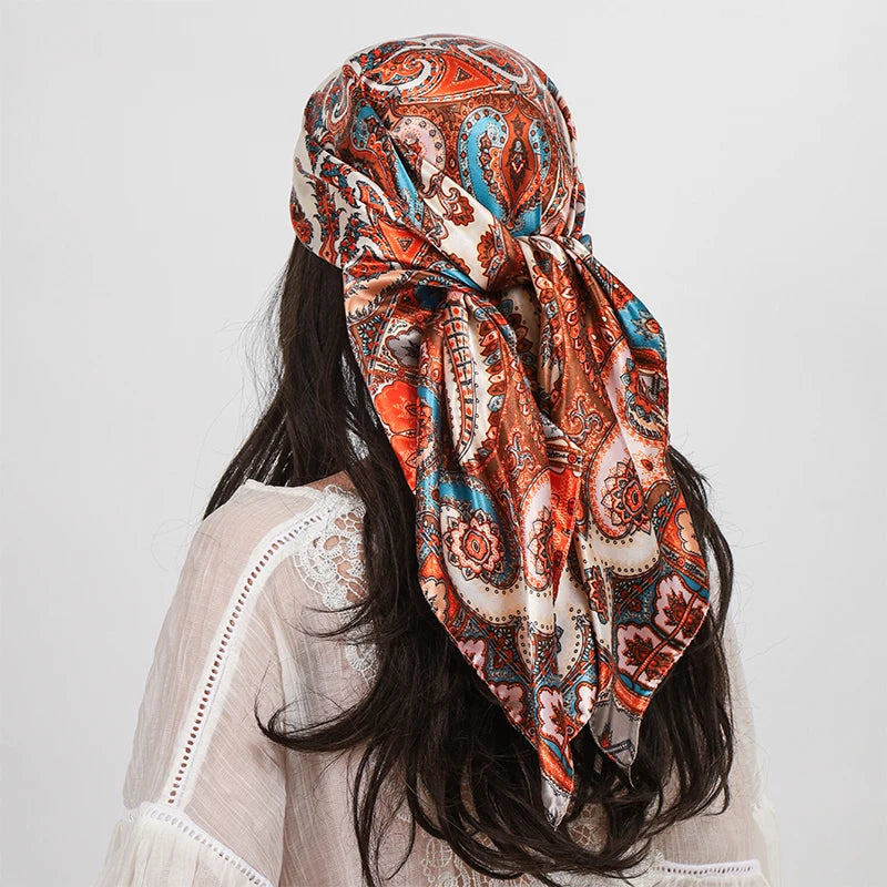 A woman wearing an orange and blue paisley silk shawl scarf tied around her neck, with long dark hair.