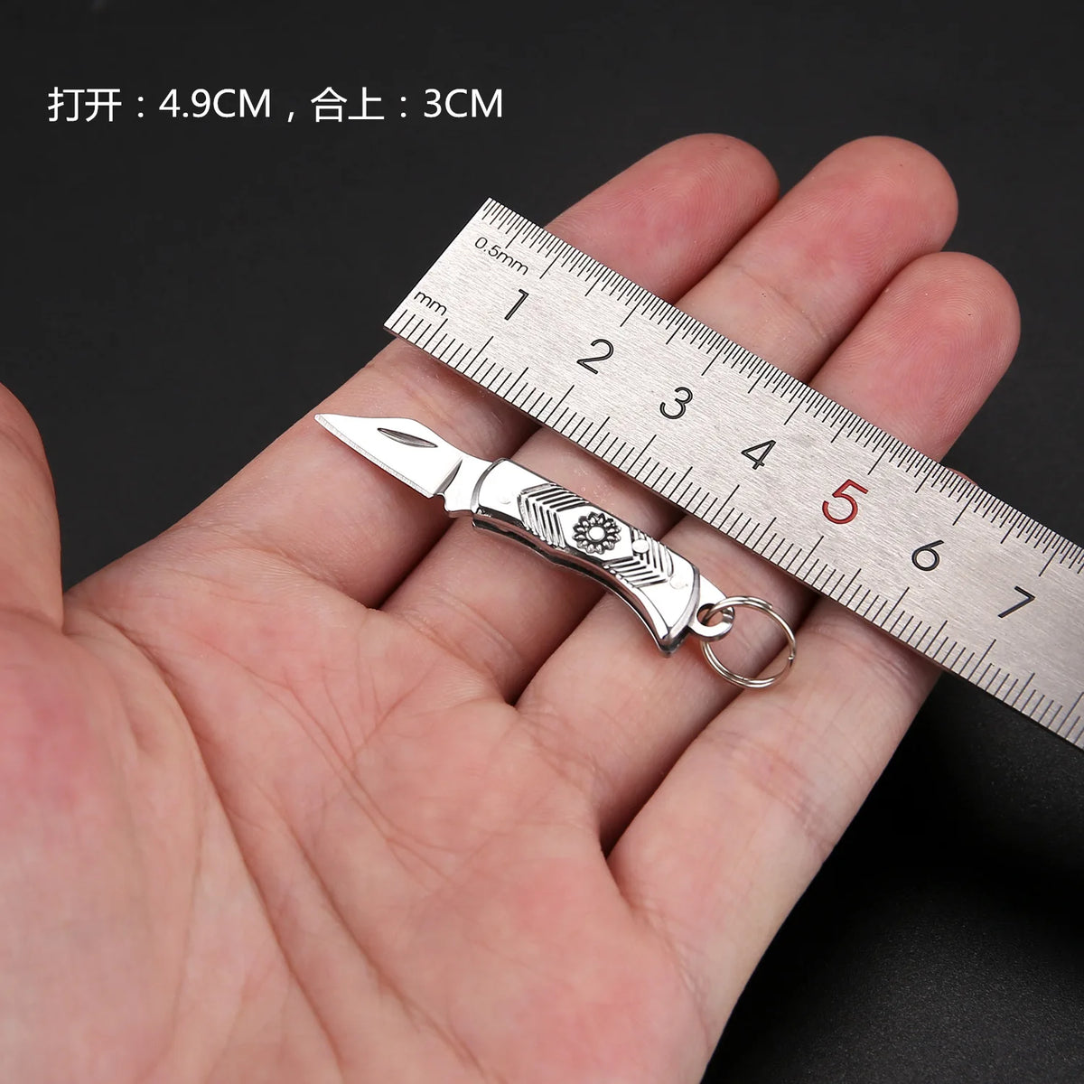 Un mini cuchillo llavero plegable de latón se muestra junto a una regla para escala.