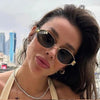 A woman wearing classic oval metal sunglasses outdoors with dark hair.