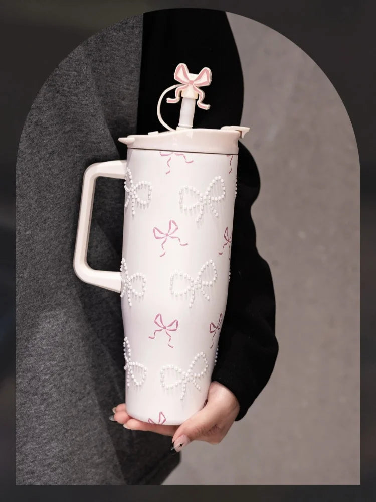 A white insulated thermos mug with pink floral inlay details is held against a dark gray fabric.