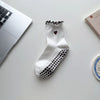 White yoga socks with black polka dots and a heart embroidery resting on a white surface.