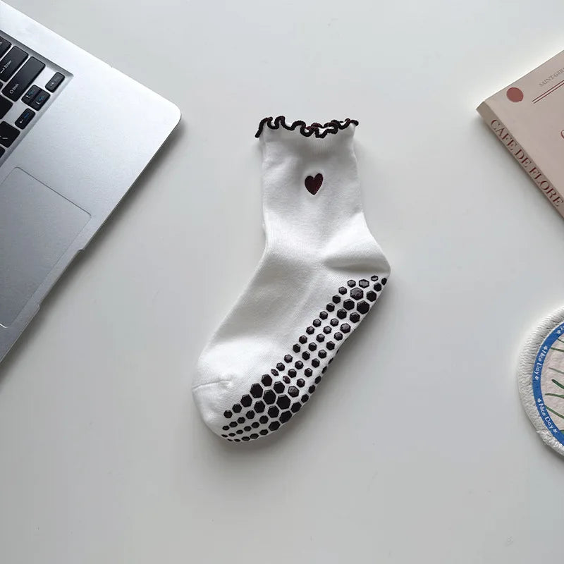 White yoga socks with black polka dots and a heart embroidery resting on a white surface.