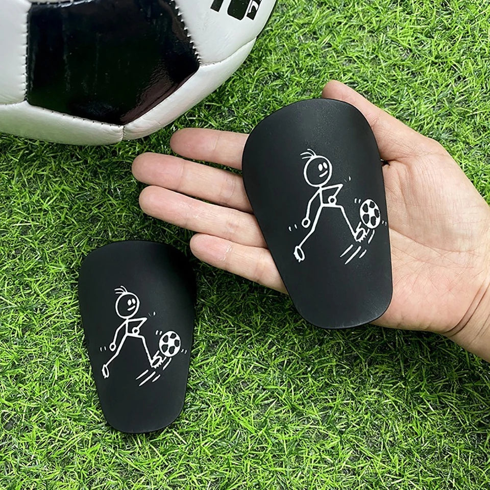 A hand holds a black mini wear-resistant shin guard for soccer, showing a stick figure running pose.