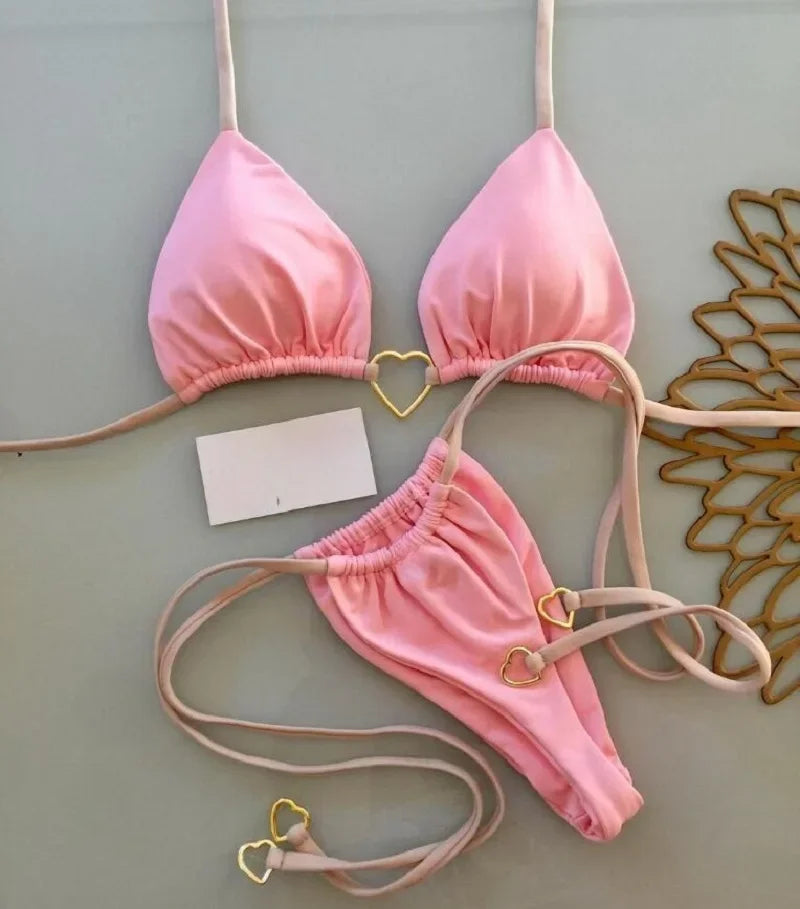 Pink halter bikini set displayed on a light gray wall.