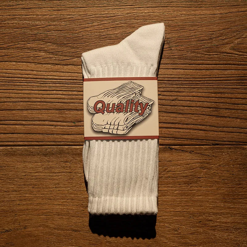 A white tube sock with a brown waistband featuring the word Quality printed on it.
