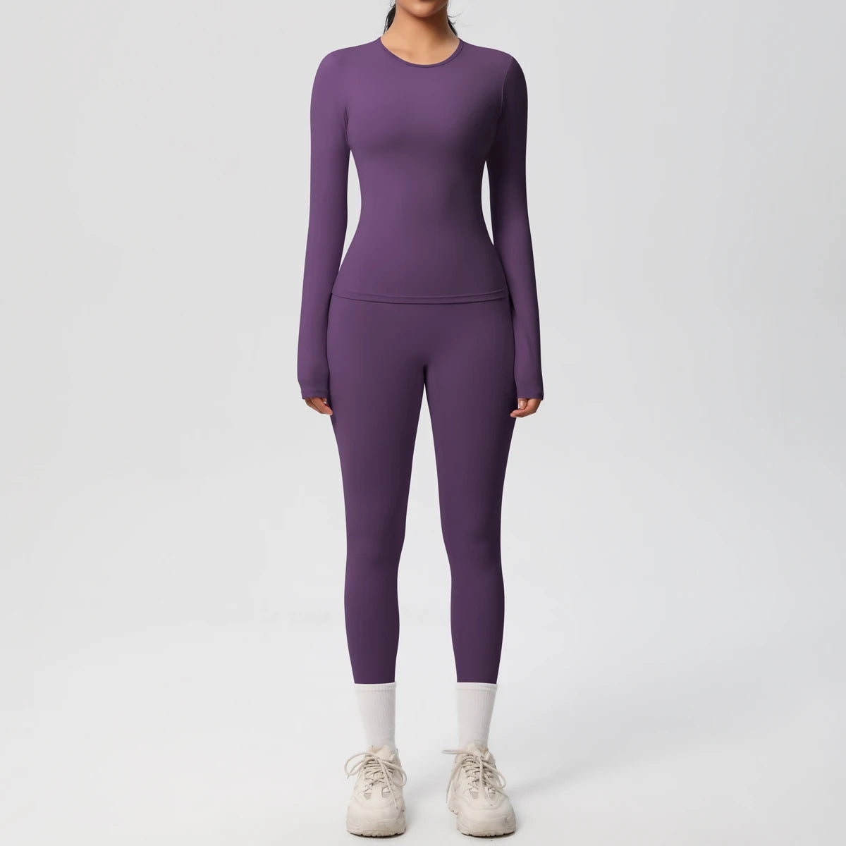 A woman wearing a long-sleeved purple performance yoga and gym set with matching leggings and white socks.