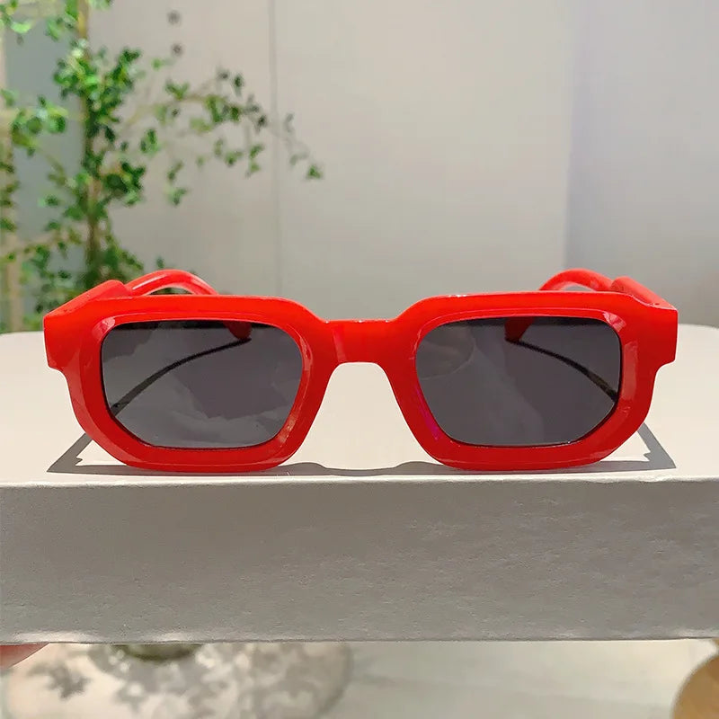 Lunettes de soleil rectangulaires rétro rouge vif posées sur une surface blanche.