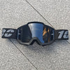 Une paire de lunettes de moto tout-terrain et ATV noires posées sur une surface grise texturée.