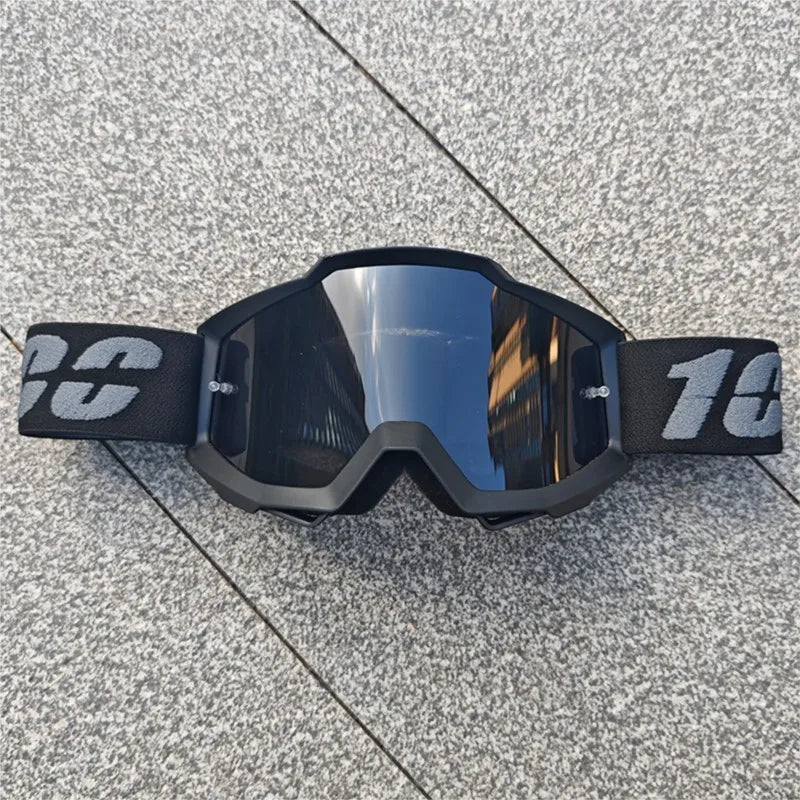 Une paire de lunettes de moto tout-terrain et ATV noires posées sur une surface grise texturée.
