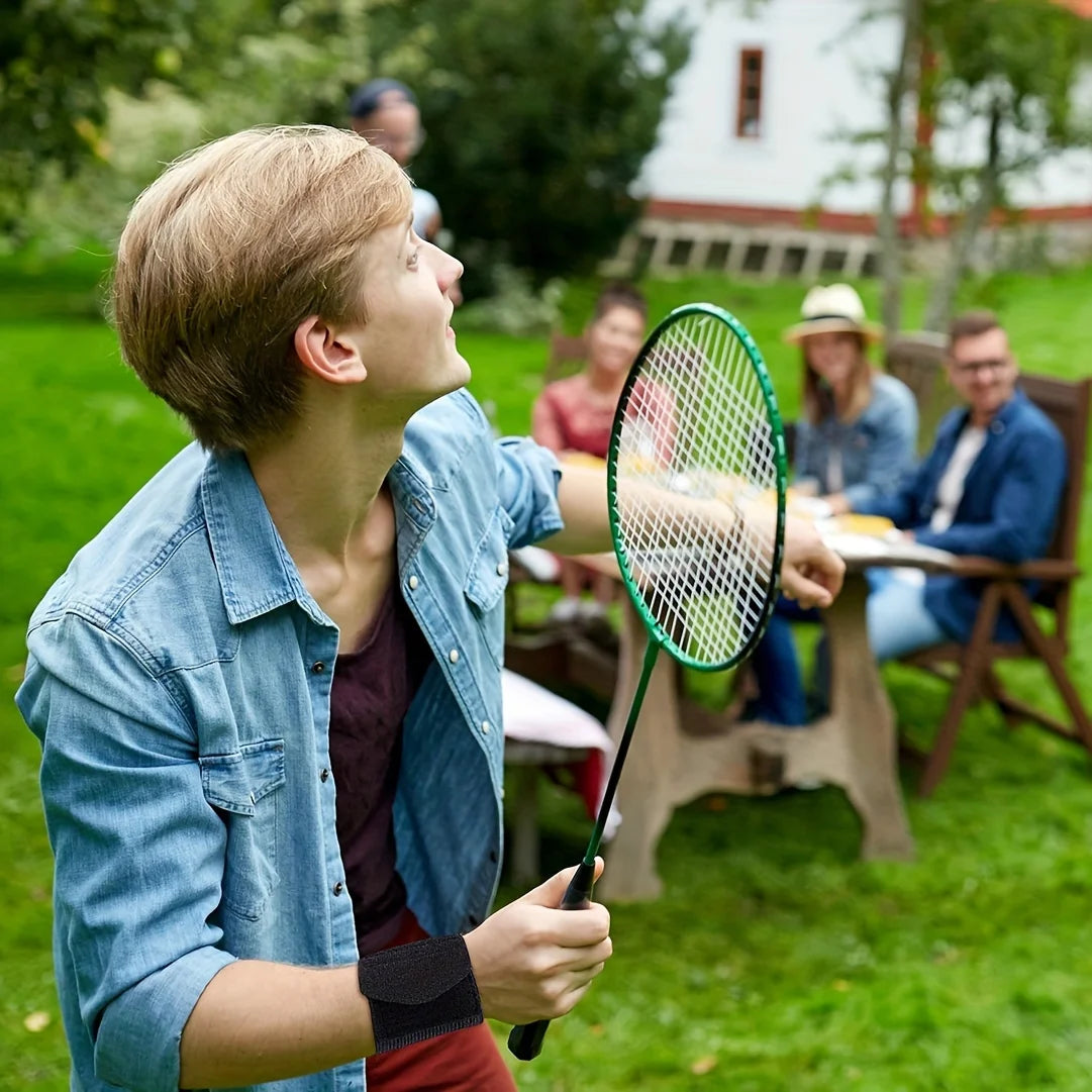 A young man in a denim shirt is holding a tennis racket outdoors while other people watch.