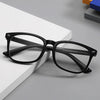 A pair of black reading glasses with dark frames and clear lenses resting on a white surface.