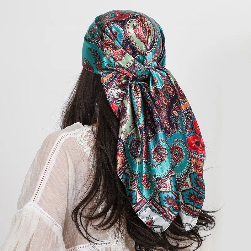 A woman wearing a teal and red paisley silk shawl scarf tied around her neck, shown from the back.