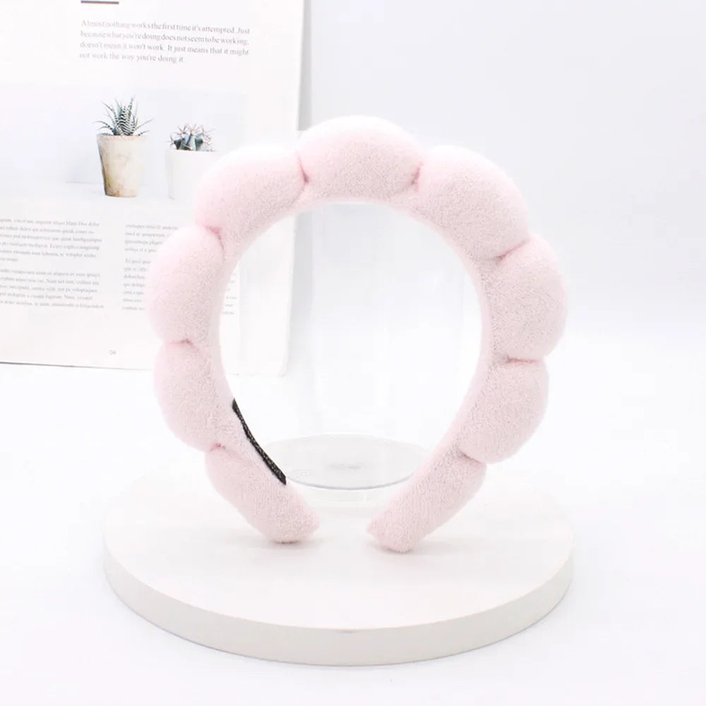 A pink sponge terry cloth headband for hair styling displayed on a white stand.