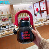 Una mano sostiene una botella de agua aislada negra con tapa y pajita rojas, etiquetada FUN SUPPLY CHAIN.