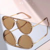 A pair of classic gradient aviator sunglasses with gold-toned frames and amber lenses resting on a light surface.