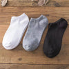 Tres calcetines de tobillo en blanco, gris y negro están dispuestos sobre una superficie de madera.