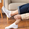 A person wearing white breathable ankle socks and dark blue jeans is shown indoors.