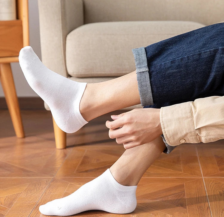 A person wearing white breathable ankle socks and dark blue jeans is shown indoors.