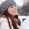Una mujer sonriente vistiendo una diadema de punto gris y un abrigo blanco de invierno, mirando hacia un lado.