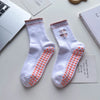 Paire de chaussettes de yoga blanches avec broderie rose et adhérence antidérapante sur une surface blanche.