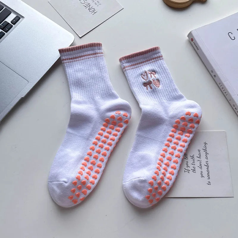 Paire de chaussettes de yoga blanches avec broderie rose et adhérence antidérapante sur une surface blanche.