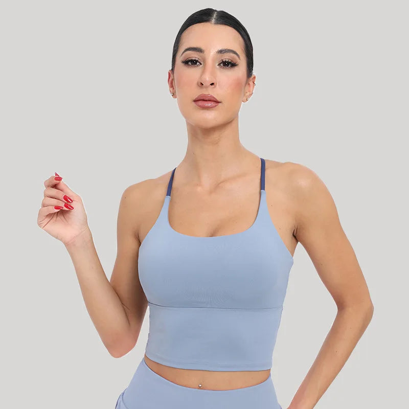 A woman models a light blue summer strappy yoga sports bra with built-in padding.