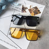 A pair of amber-tinted oversized square sunglasses resting on a white paper with nature photos.