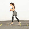 A woman in athletic wear performs agility drills on a track with yellow markers.