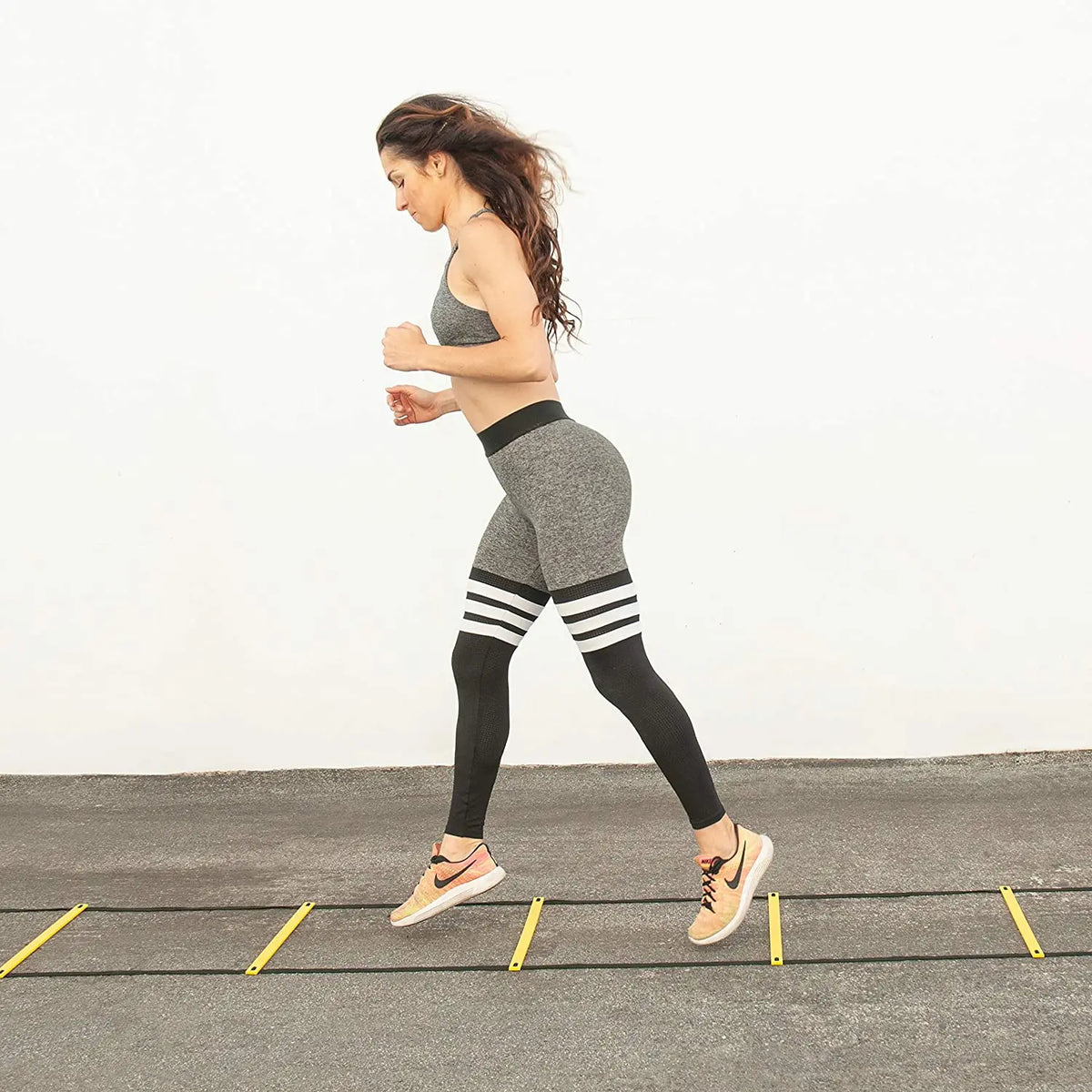 A woman in athletic wear performs agility drills on a track with yellow markers.