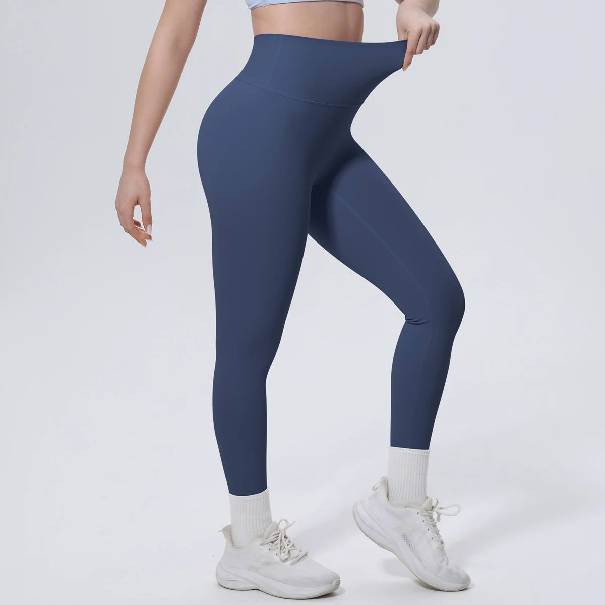 A model wearing navy blue high-waisted yoga leggings and white socks, standing against a light background.
