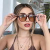 A woman models vintage square sunglasses with a double bridge against a bright background.