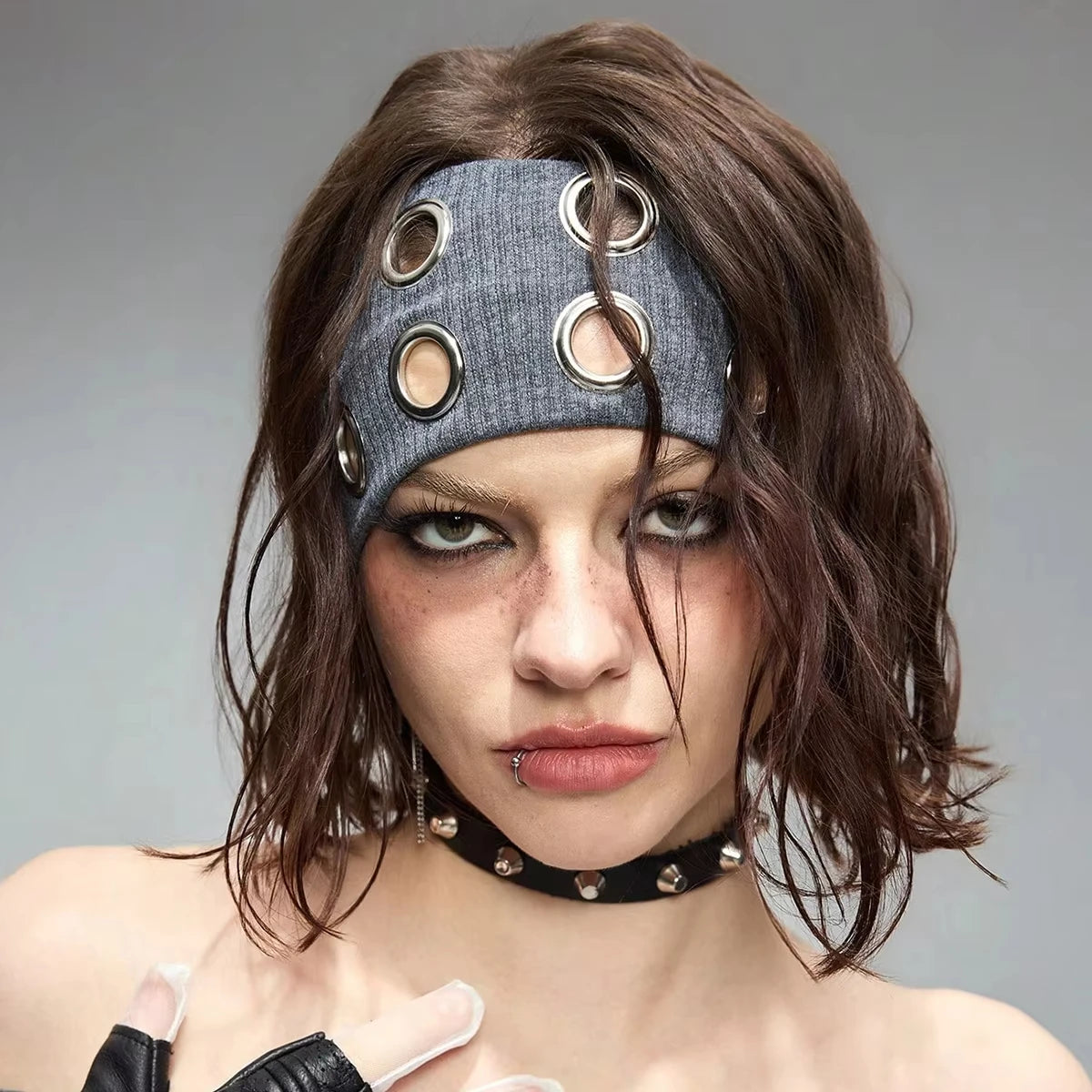 Une femme portant un bandeau en œillet punk grunge gris foncé avec des anneaux argentés dans ses cheveux foncés.