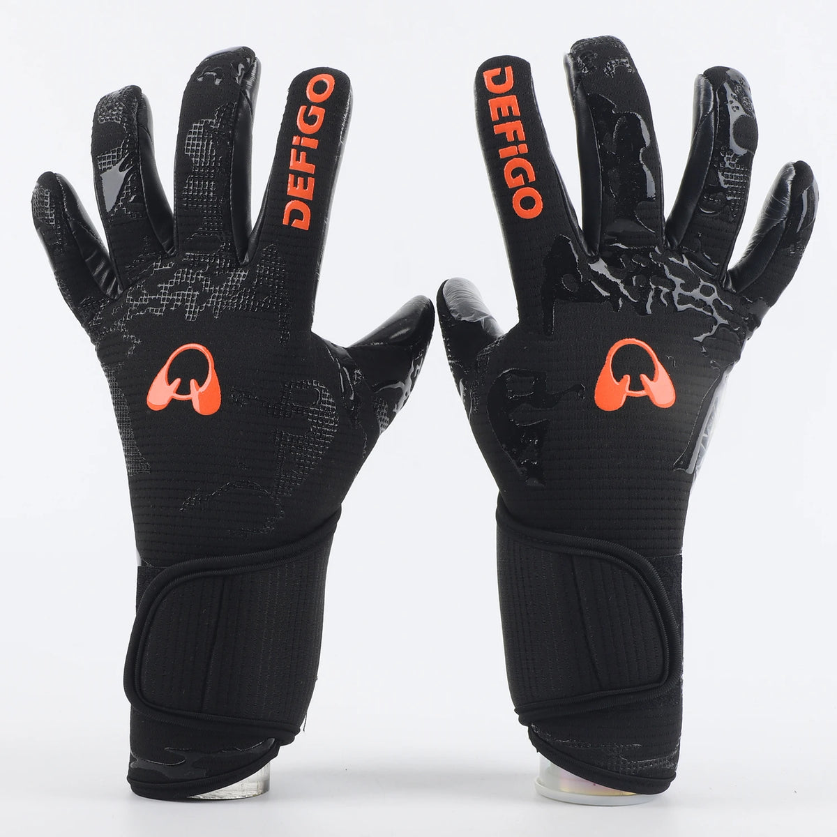 A pair of black professional football goalkeeper gloves with orange Defigo branding.